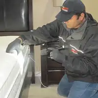 Bed bug inspection technician checking a mattress and bed frame for signs of infestation in Overland Park, KS