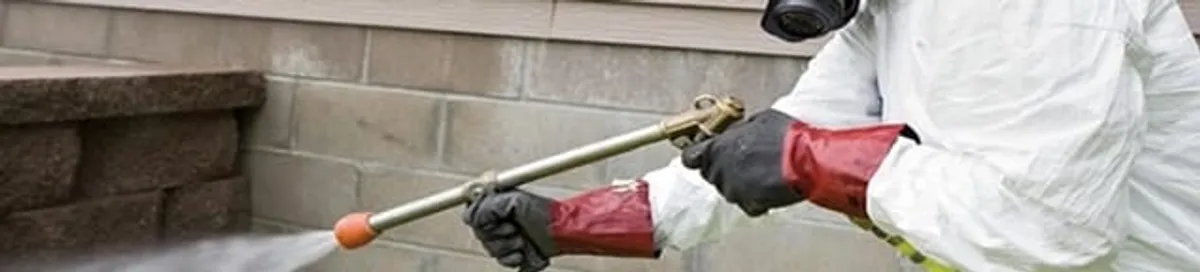 Pest control technician applying exterior insect treatment along a home foundation in Overland Park, KS