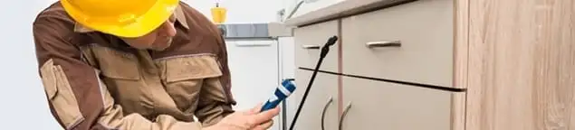 Roach exterminator applying treatment under kitchen cabinets in Overland Park, KS