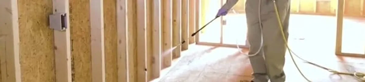 Termite treatment technician applying spray along framing and unfinished walls in Overland Park, KS