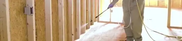 Termite treatment technician applying spray along framing and unfinished walls in Overland Park, KS